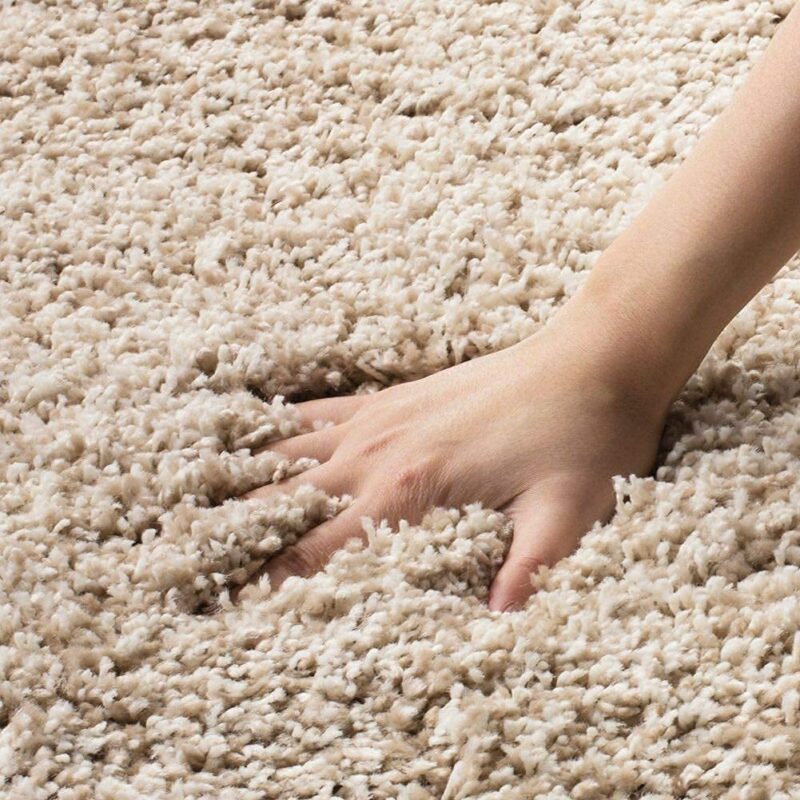 Soft beige polyester carpet with hand demonstrating plush texture, ideal for living room decor.