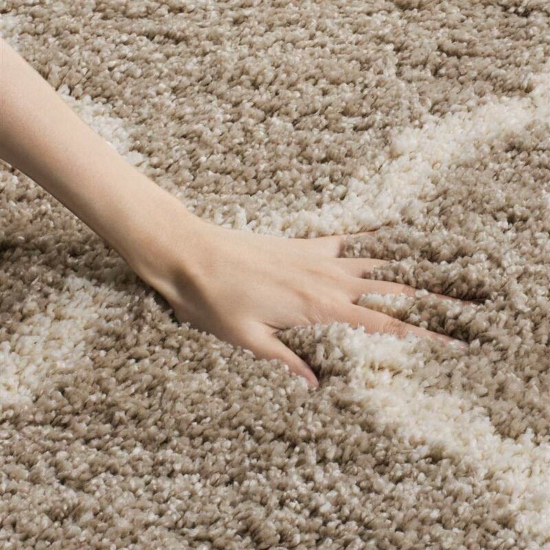 Close-up of a hand touching a soft, beige Moroccan design polyester carpet.